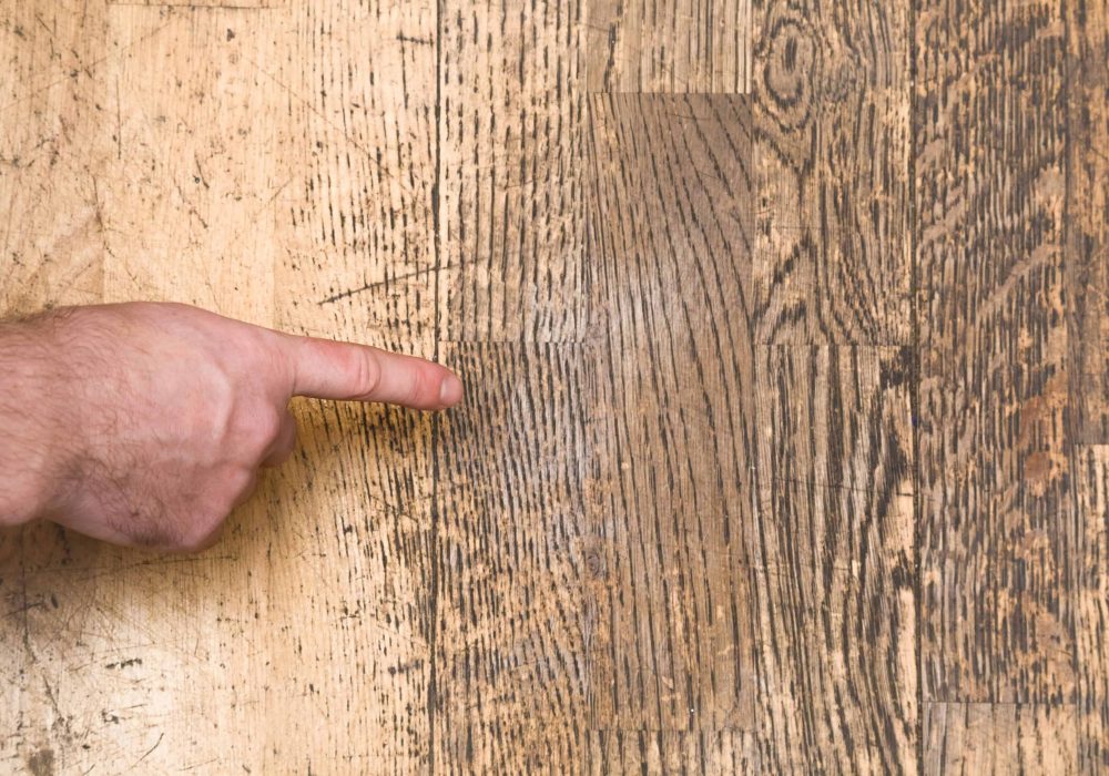 Man's hand pointing to the old scratched wooden floor in the room. Problems and solutions concept.