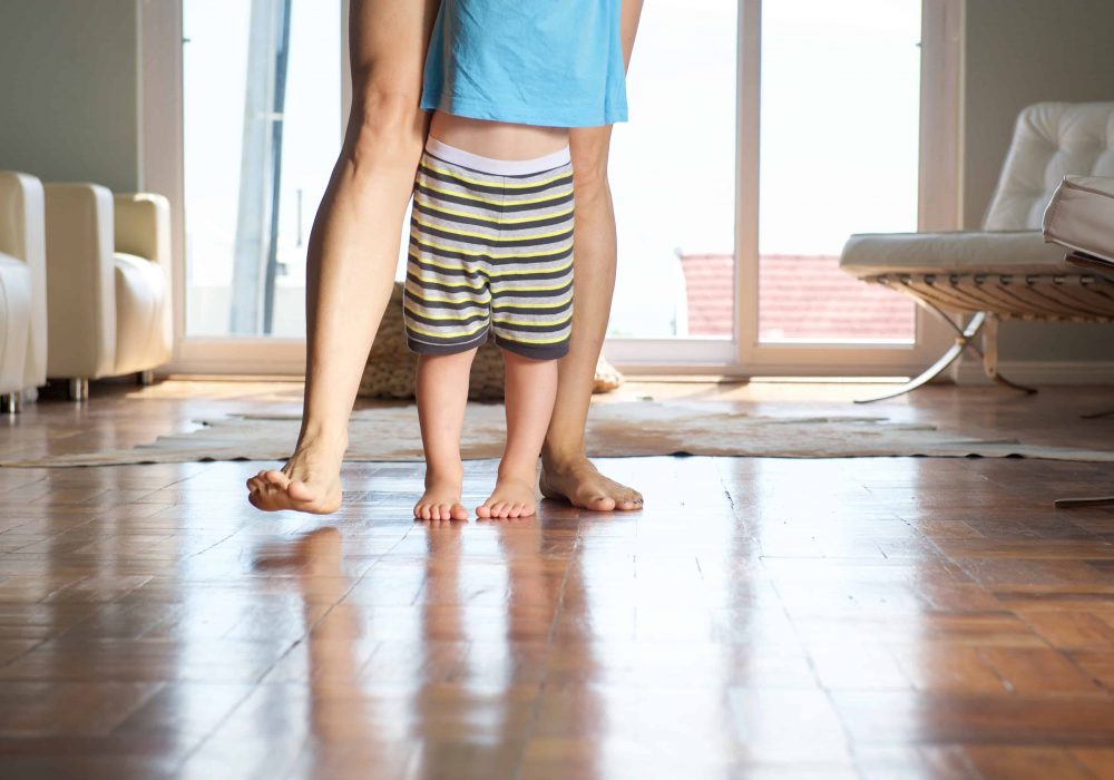 Mother walking with little boy at home on wood floor