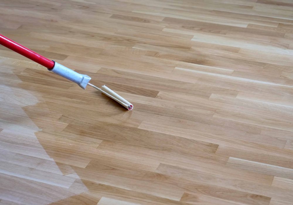 Varnishing lacquering an oak parquet floor by paint roller first layer.
